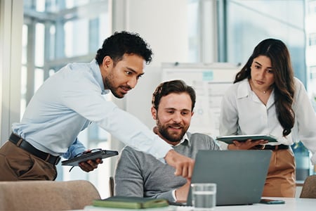 Three colleagues collaborating on laptop in modern office