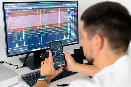 Trader viewing stock charts on phone and computer screens