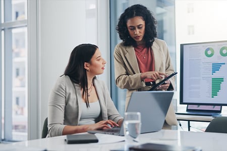 Two professionals collaborating with laptop and tablet in office